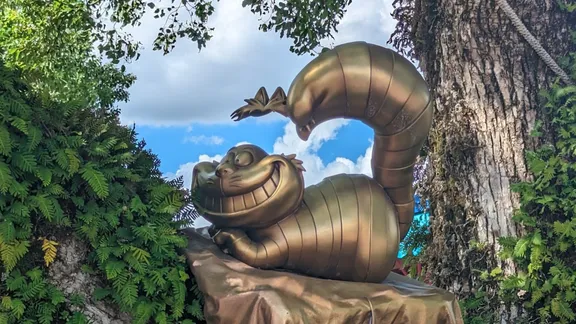 Bronze sculpture of a smiling, cartoon-like curled creature with a raised segmented tail, surrounded by tropical foliage.