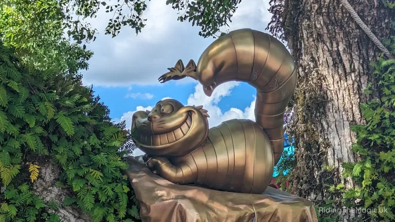 Bronze sculpture of a smiling, cartoon-like curled creature with a raised segmented tail, surrounded by tropical foliage.