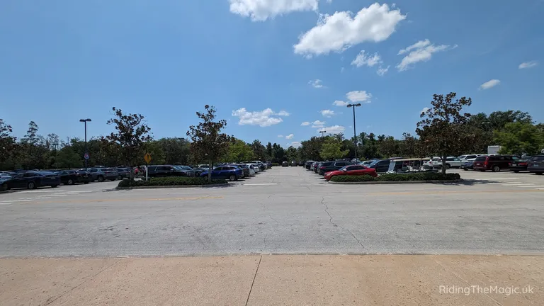 Large car park with parked cars, trees and a blue sky with clouds