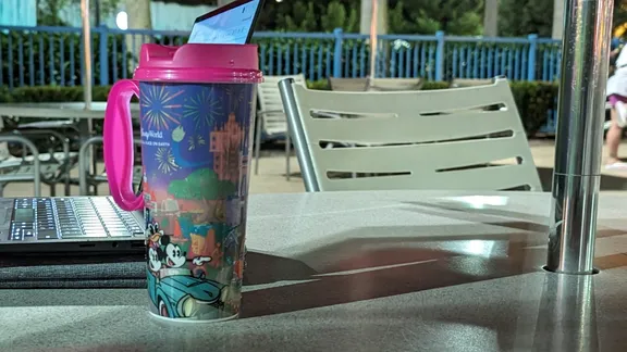 Disney-themed travel mug with pink lid and handle on a table outdoors