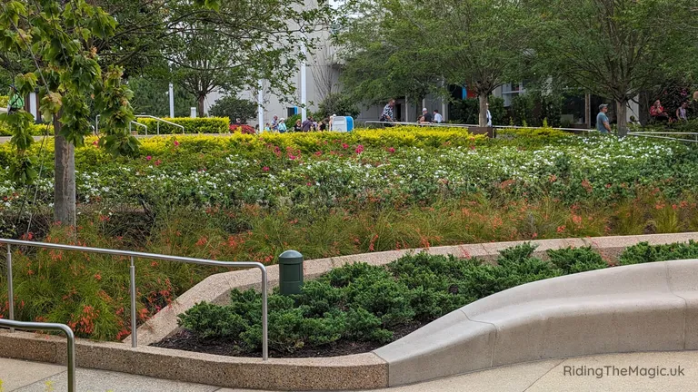 Landscaped garden with flower beds, trees and a curved stone bench beside a path