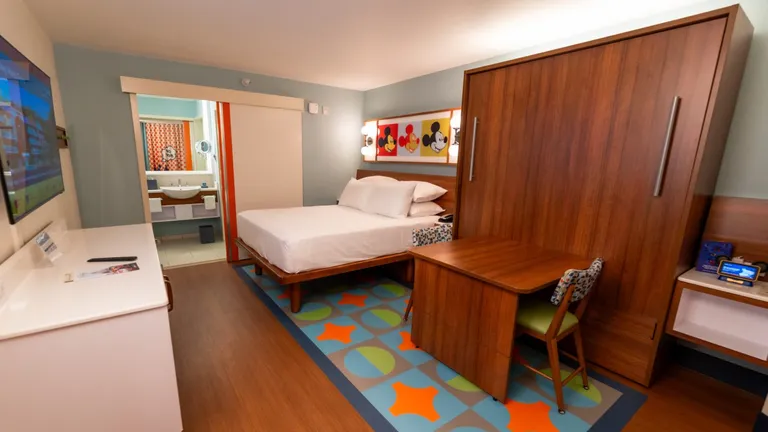 A Disney hotel room with a bed, desk, and a colorful rug