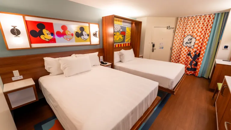 Two twin beds in a Disney hotel room with Mickey Mouse artwork on the walls