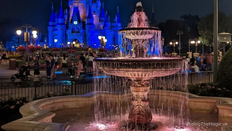 Cinderella Castle illuminated blue behind a tiered fountain at night in a crowded theme park.