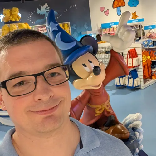 Selfie of a man wearing glasses beside a Mickey Mouse statue in a wizard costume inside a shop.