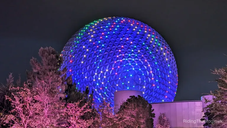 Geodesic dome illuminated with blue, green and red lights at night, partly obscured by trees.