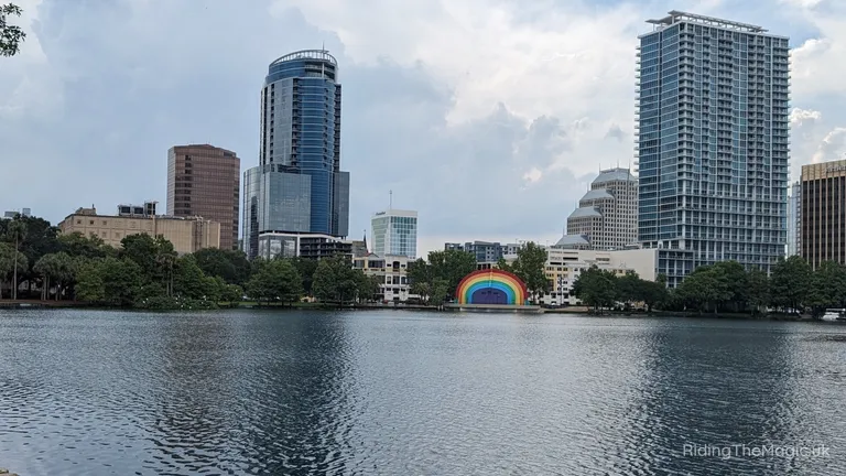 City skyline across a lake, featuring high-rise buildings and a rainbow-coloured sculpture on the waterfront.