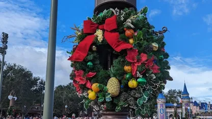 Festive Christmas wreath decorated with red bows, fruit, pinecones and evergreen foliage on a street lamp.