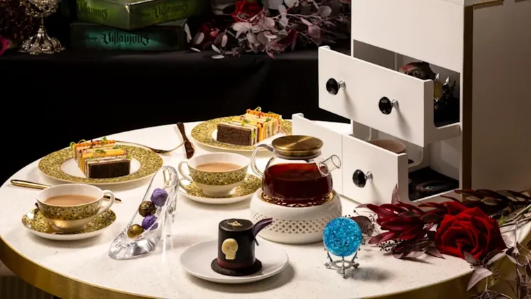 Tea table set with decorated teacups, teapot, coffee cup, pastries and a blue decorative ornament.
