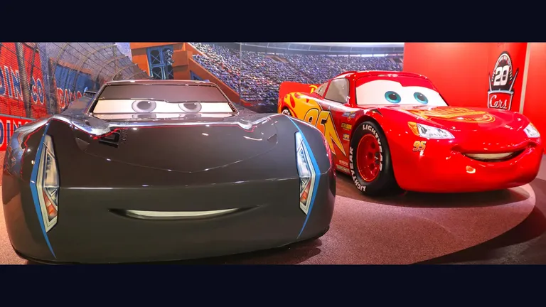 Lightning McQueen and a dark grey car from Cars displayed in a racing stadium.