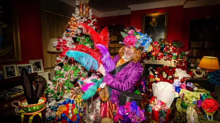 Person in a purple coat beside a Christmas tree covered in colourful decorations and feathers.