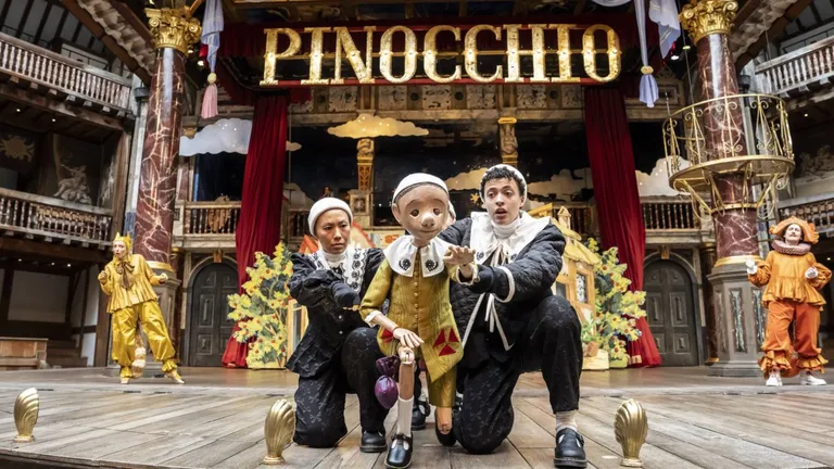 Puppet Pinocchio with two performers on stage beneath a large “PINOCCHIO” sign.