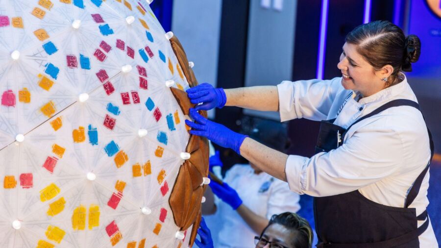 A woman in a white shirt and apron decorates a large spherical object