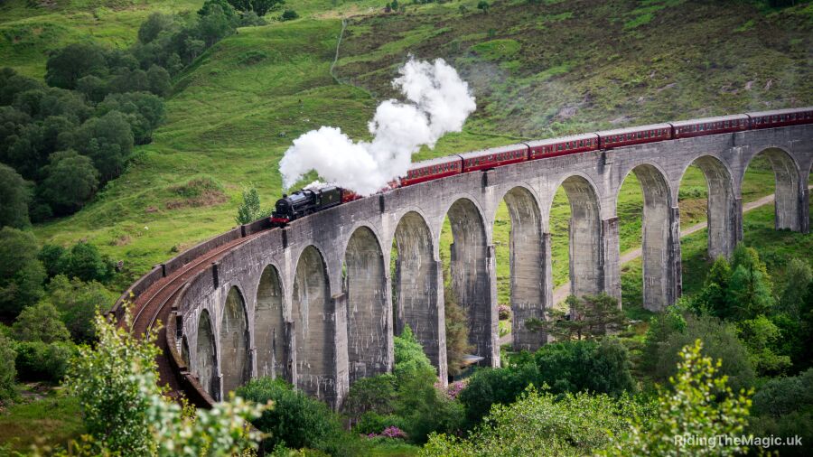 A steam train crosses the Glenfinnan Viaduct in Scotland, surrounded by lush greenery