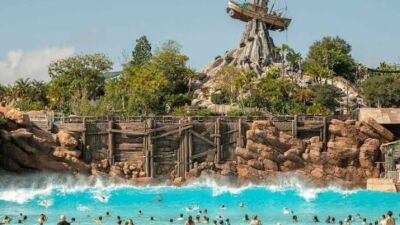 A wave pool with people swimming in it and a boat on top of a rock
