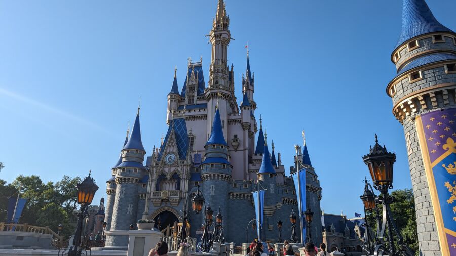 Disney's Magic Kingdom Castle on a sunny day with blue sky and people walking around