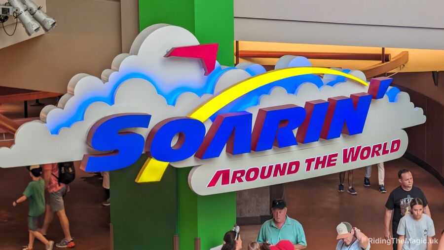 People walk past a sign for the Soarin' ride at Disney World