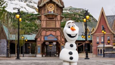 Olaf from Frozen standing in front of a clock tower in a theme park