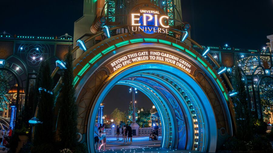 Epic Universe entrance at night with glowing lights and people walking through the archway