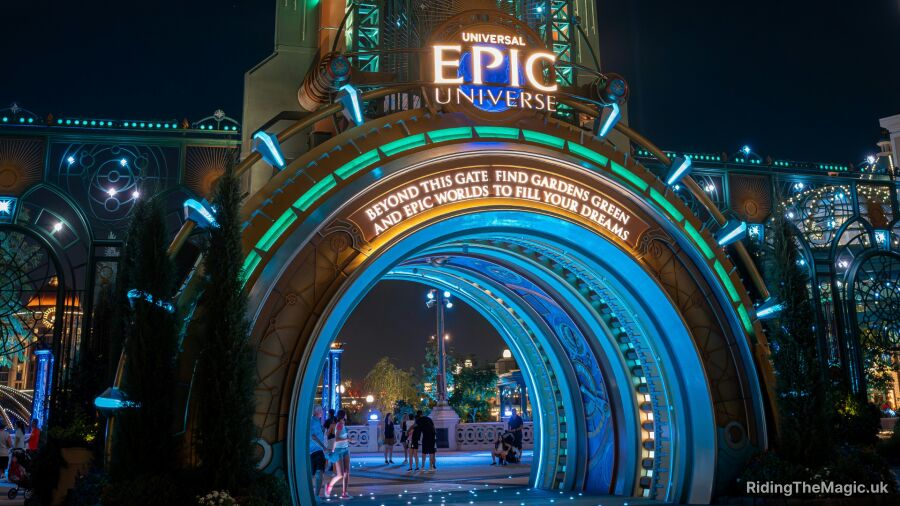 Epic Universe entrance at night with glowing lights and people walking through the archway