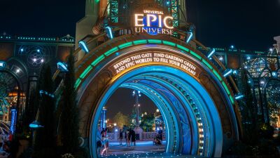 Epic Universe entrance at night with glowing lights and people walking through the archway