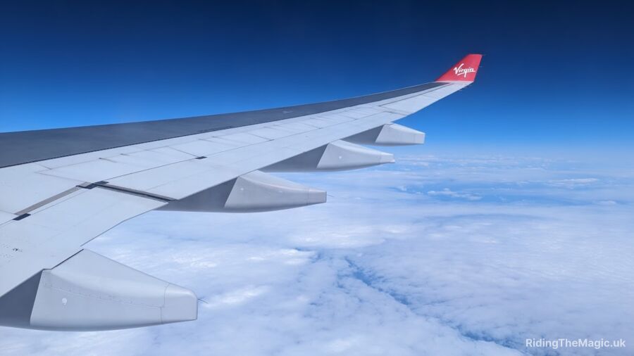 Virgin Atlantic airplane wing flying above the clouds with a blue sky in the background