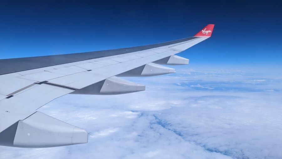 Virgin Atlantic airplane wing flying above the clouds with a blue sky in the background