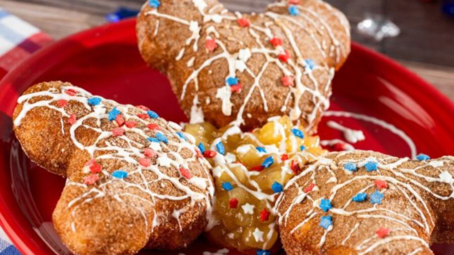 Mickey shaped donuts with white icing and red, white, and blue sprinkles on a red plate