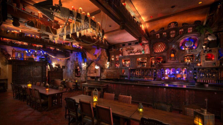 A dimly lit bar with wooden tables, chairs, and a bar counter with bottles