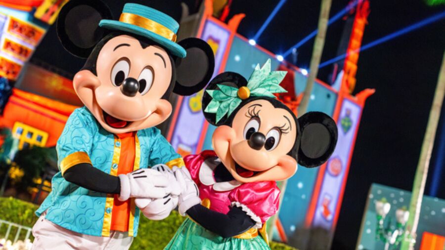 Mickey and Minnie Mouse wearing Hawaiian outfits and holding hands in front of a ride
