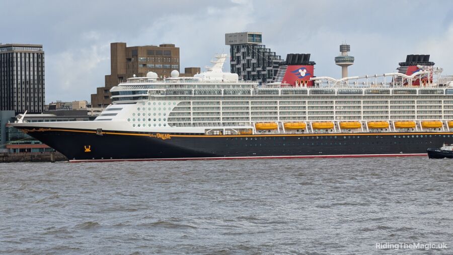 A large cruise ship with a Disney logo sails on the water near a city