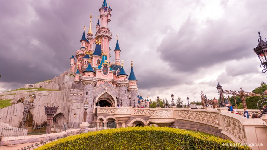 Disneyland Paris castle with blue and pink turrets, a bridge, and a cloudy sky