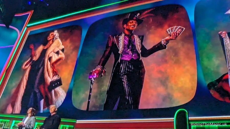 A man dressed in a purple suit is holding cards and a wand on a stage
