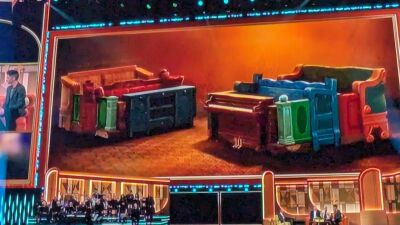 A colorful image of a sofa and piano on stage with a band in the background