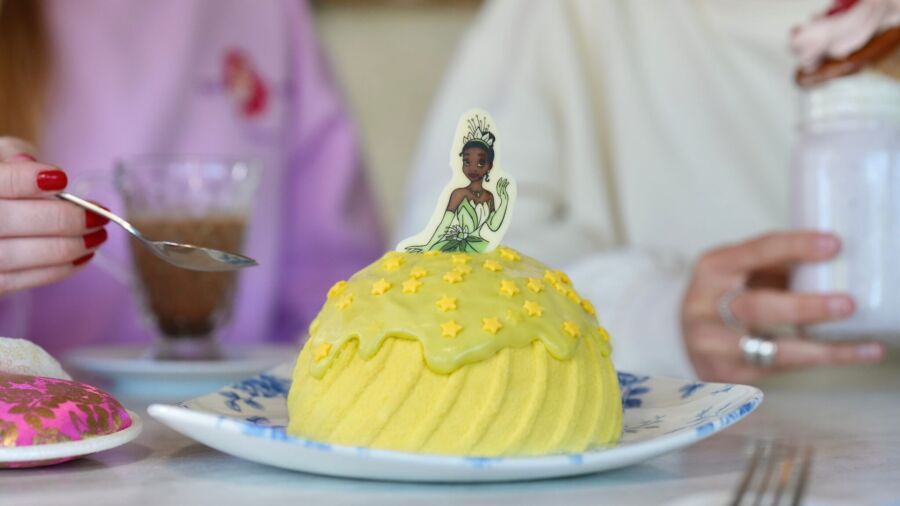 A closeup of a yellow cake with a Tiana figurine on top of it
