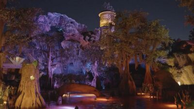 Nighttime view of Tiana's Bayou Adventure ride at Disney World, featuring purple lights and trees