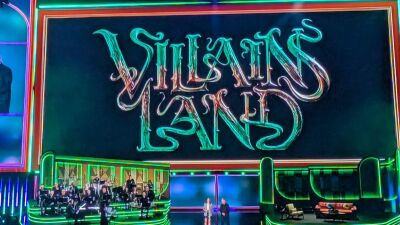 Villains Land logo on a stage with a band and two people standing