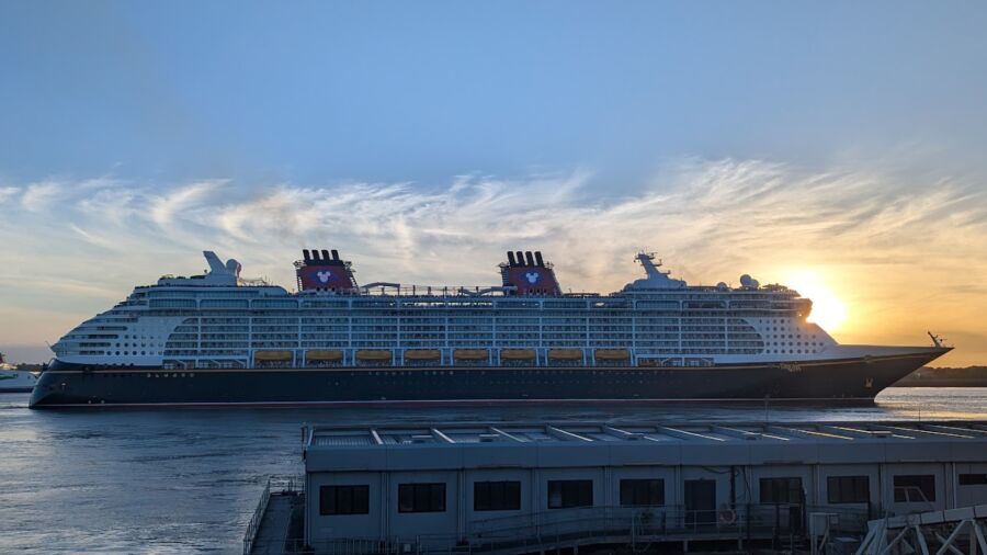 A large Disney cruise ship sails into a port at sunset