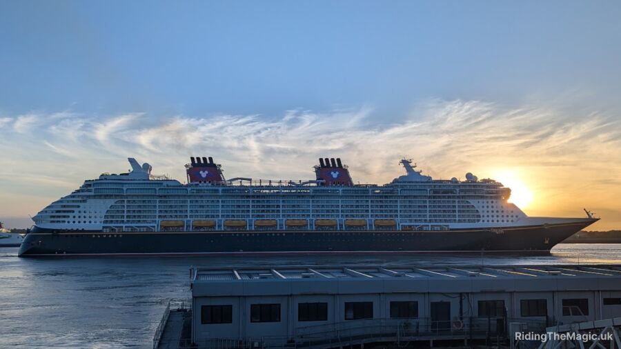 A large Disney cruise ship sails into a port at sunset