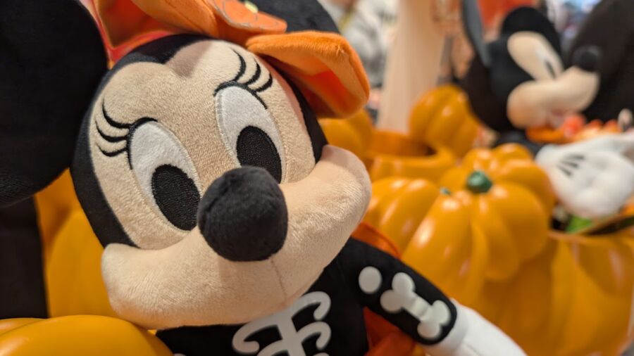 A Halloween-themed Minnie Mouse plush sits next to pumpkins in a store