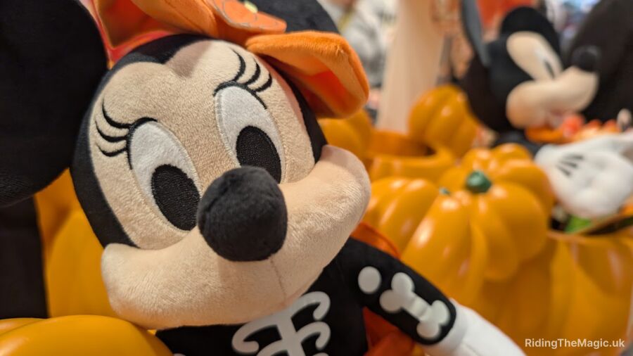 A Halloween-themed Minnie Mouse plush sits next to pumpkins in a store