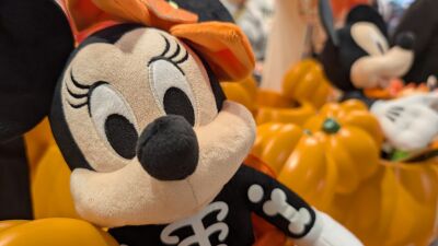 A Halloween-themed Minnie Mouse plush sits next to pumpkins in a store