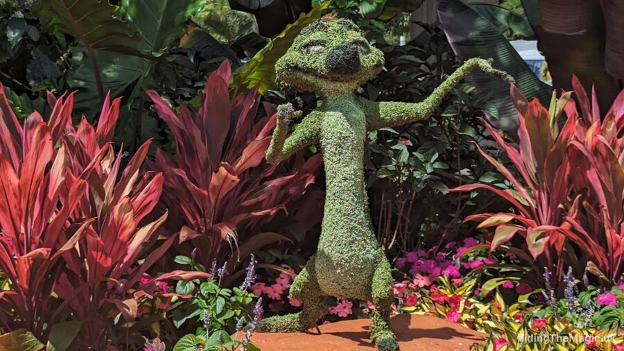 A garden with a green topiary of a lizard standing in the middle