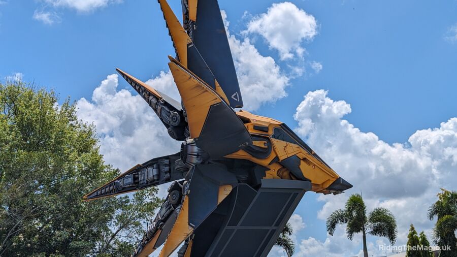 A yellow and black robot stands tall against a blue sky with white clouds