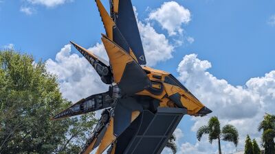 A yellow and black robot stands tall against a blue sky with white clouds