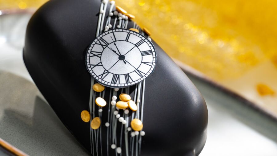 A black cake decorated with a clock and gold coins on a plate