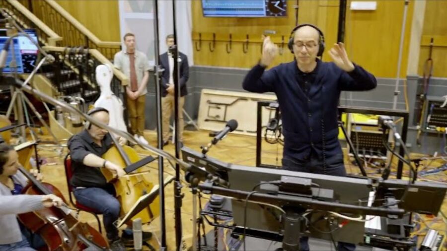 A man is conducting a band while wearing headphones in a recording studio
