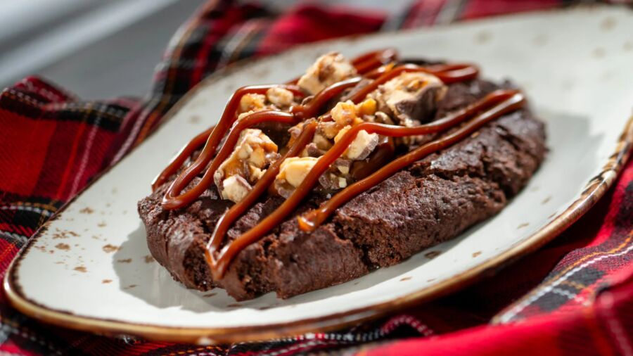 A chocolate cookie with caramel and nuts on a white plate with a red cloth