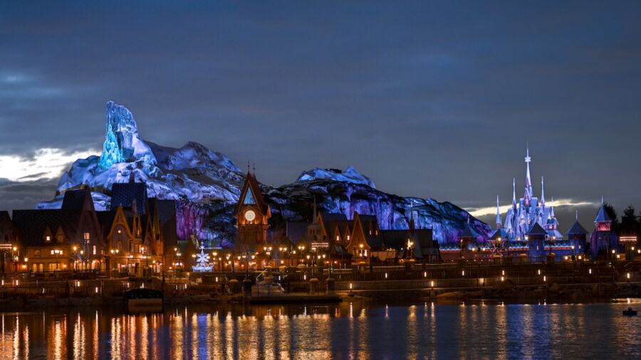Night view of a Disney park with a castle and mountains in the background